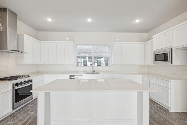 kitchen featuring sink, stainless steel appliances, white cabinets, a kitchen island, and wall chimney exhaust hood