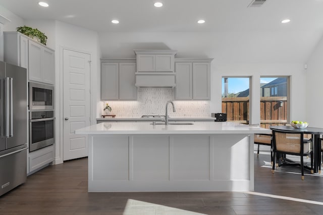 kitchen with appliances with stainless steel finishes, backsplash, sink, dark hardwood / wood-style floors, and an island with sink