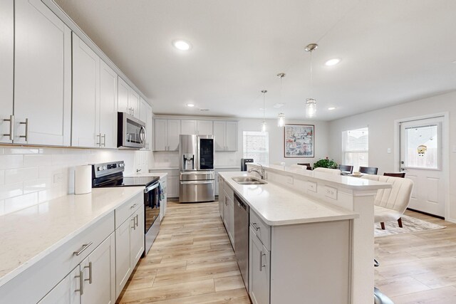 kitchen with a breakfast bar area, a kitchen island with sink, stainless steel appliances, a sink, and pendant lighting