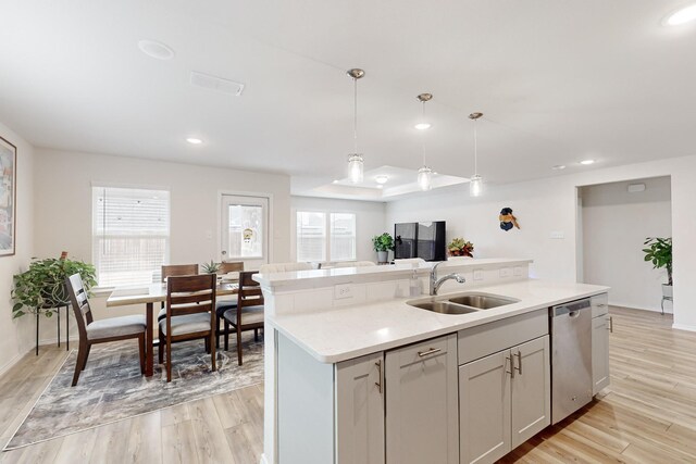 kitchen featuring hanging light fixtures, light wood-style flooring, a kitchen island with sink, a sink, and dishwasher