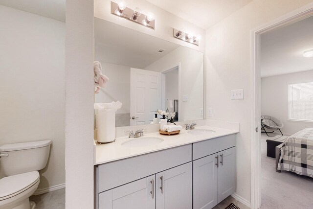 full bath with ensuite bathroom, double vanity, a sink, and toilet