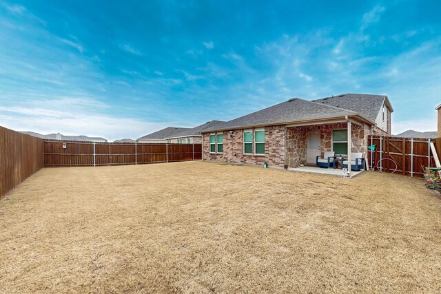 back of house with brick siding, a patio, a shingled roof, a lawn, and a fenced backyard