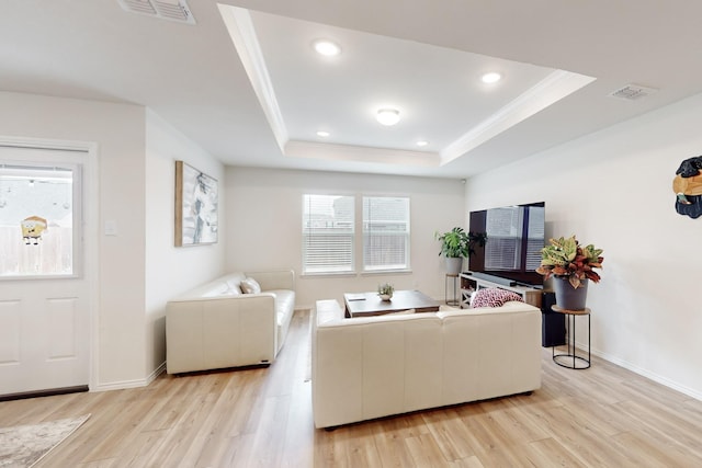 living room with light wood-type flooring, a raised ceiling, visible vents, and baseboards