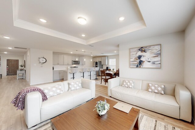 living area with recessed lighting, light wood-style flooring, a tray ceiling, and ornamental molding