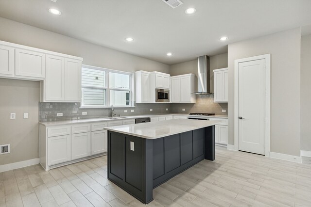 kitchen featuring white cabinets, a kitchen island, stainless steel microwave, and wall chimney range hood