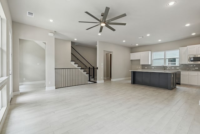 kitchen with ceiling fan, appliances with stainless steel finishes, tasteful backsplash, open floor plan, and white cabinetry