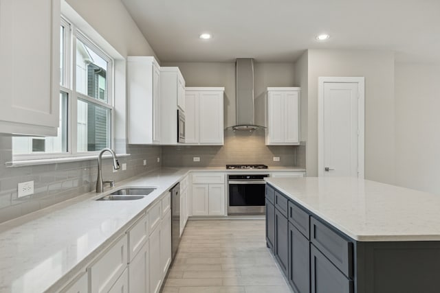 kitchen featuring light stone countertops, white cabinetry, sink, stainless steel appliances, and wall chimney range hood