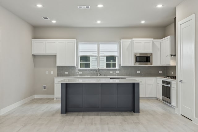 kitchen with decorative backsplash, stainless steel appliances, a center island, and white cabinets