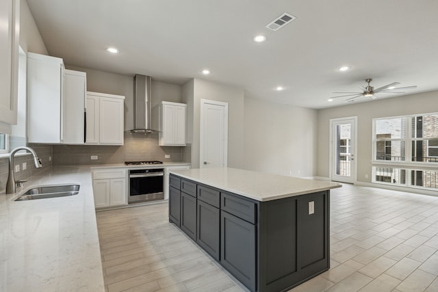 kitchen with sink, white cabinetry, a kitchen island, stainless steel appliances, and wall chimney range hood