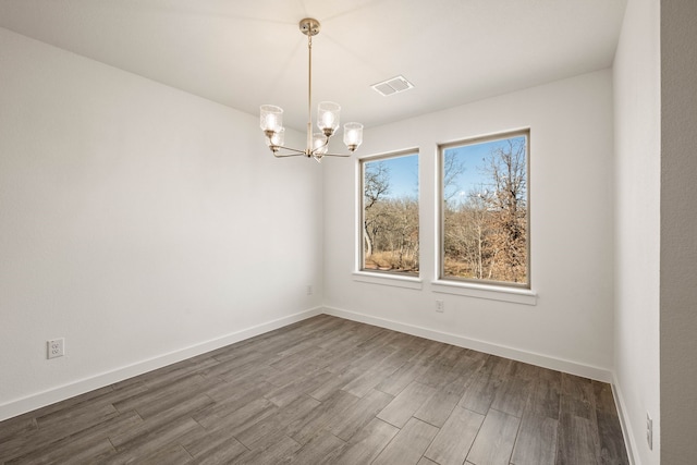 empty room featuring wood-type flooring and an inviting chandelier