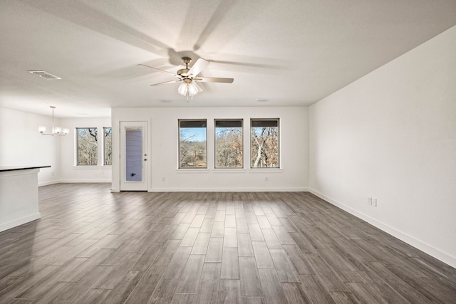 empty room with dark hardwood / wood-style flooring, ceiling fan with notable chandelier, and a textured ceiling