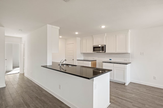 kitchen with sink, white cabinets, backsplash, light hardwood / wood-style floors, and kitchen peninsula