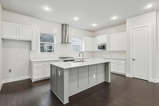 kitchen featuring an island with sink, sink, white cabinets, stainless steel appliances, and wall chimney range hood