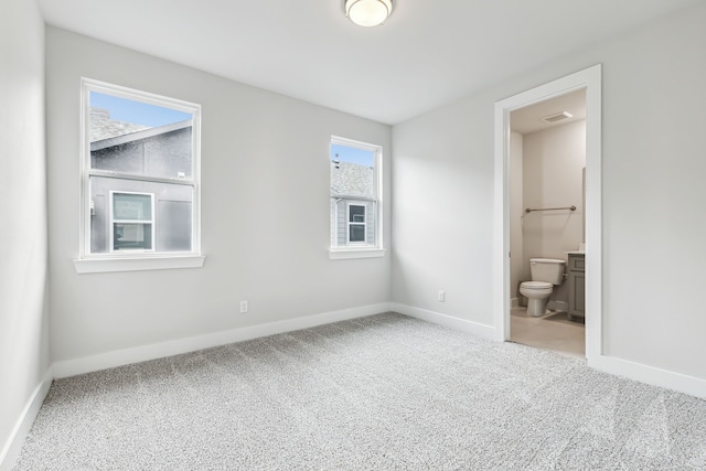 unfurnished bedroom featuring carpet flooring, ensuite bathroom, and multiple windows