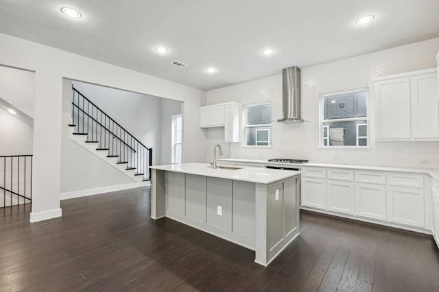 kitchen featuring a center island with sink, wall chimney exhaust hood, white cabinets, and sink