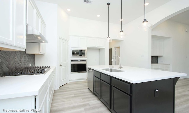 kitchen featuring sink, appliances with stainless steel finishes, a kitchen island with sink, white cabinets, and decorative light fixtures