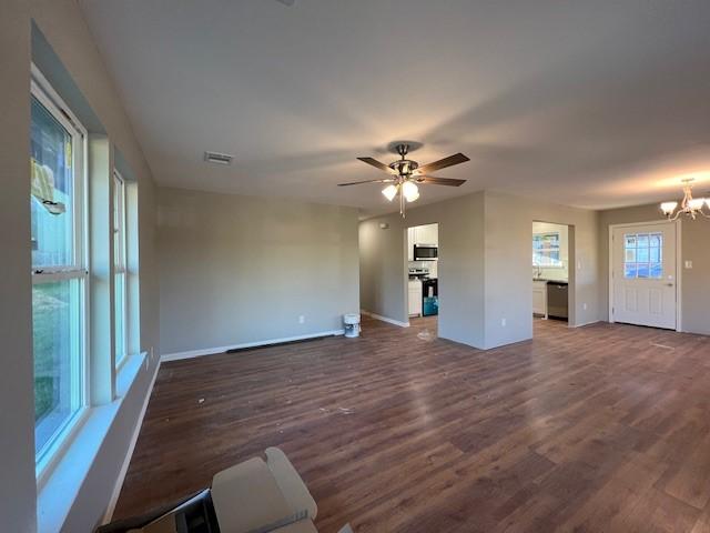 unfurnished living room with ceiling fan with notable chandelier and dark hardwood / wood-style floors