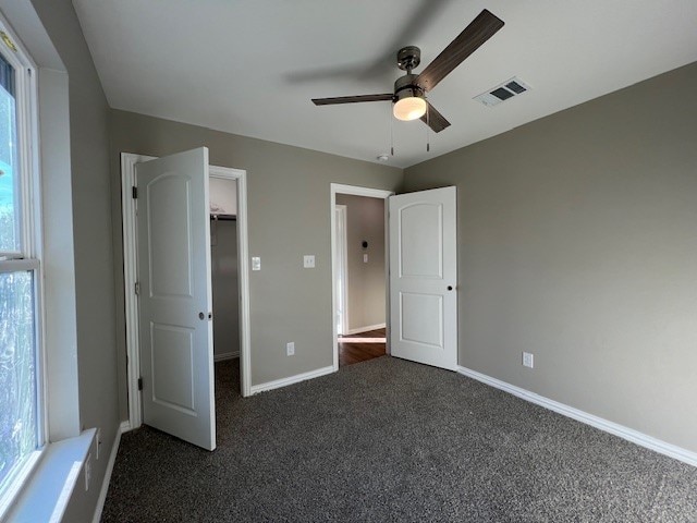 unfurnished bedroom featuring multiple windows, ceiling fan, a spacious closet, and dark carpet