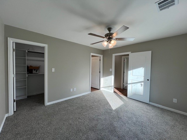 unfurnished bedroom with ceiling fan, a closet, a spacious closet, and dark carpet