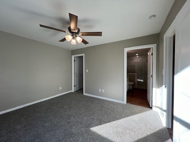 unfurnished bedroom with connected bathroom, dark carpet, and ceiling fan