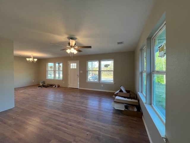 unfurnished living room with ceiling fan with notable chandelier and dark wood-type flooring