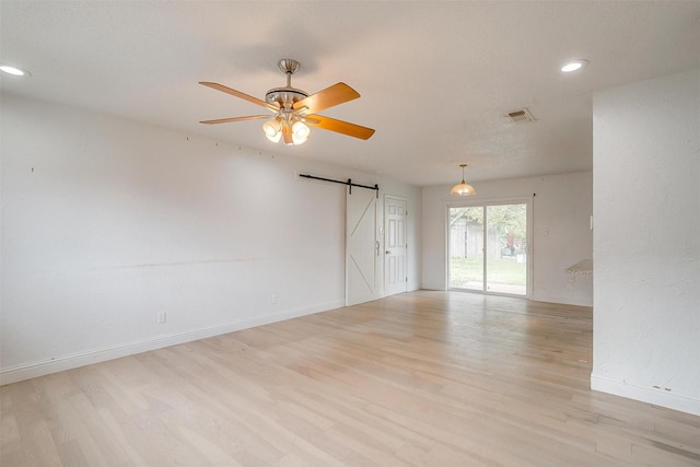 unfurnished room with a barn door, ceiling fan, and light hardwood / wood-style floors