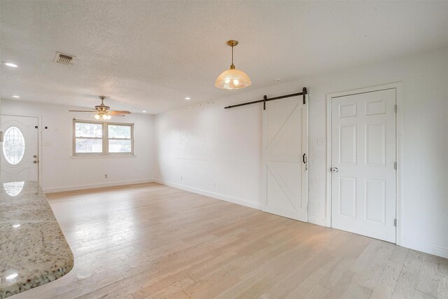 unfurnished room featuring a textured ceiling, a barn door, light hardwood / wood-style flooring, and ceiling fan