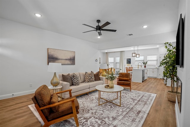 living room with ceiling fan, sink, and light wood-type flooring