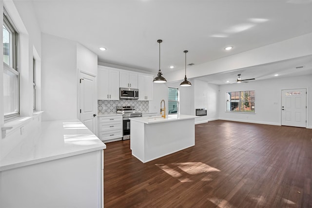 kitchen with pendant lighting, white cabinets, backsplash, stainless steel appliances, and a center island with sink