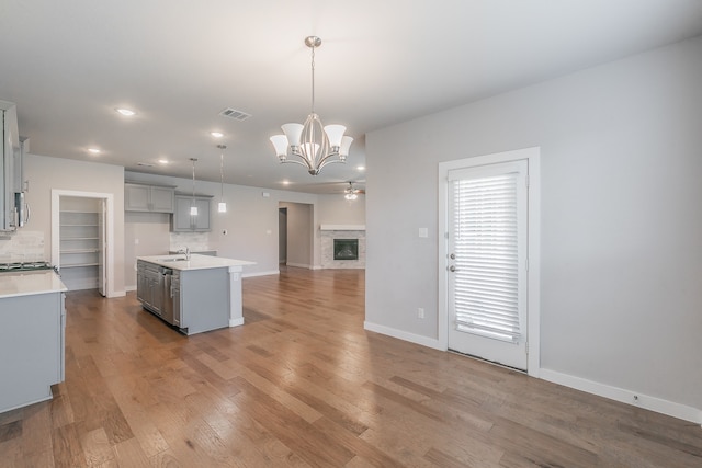 kitchen with light wood-type flooring, gray cabinetry, sink, pendant lighting, and a center island with sink