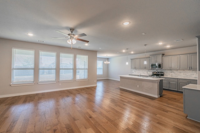 kitchen featuring gray cabinetry, stainless steel appliances, an island with sink, pendant lighting, and light hardwood / wood-style floors