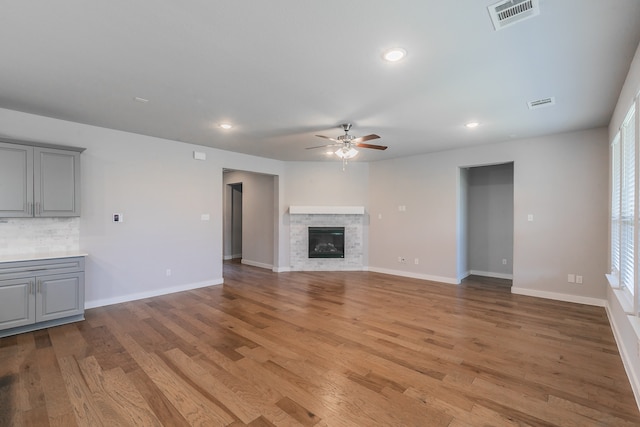 unfurnished living room featuring a stone fireplace, plenty of natural light, and light wood-type flooring