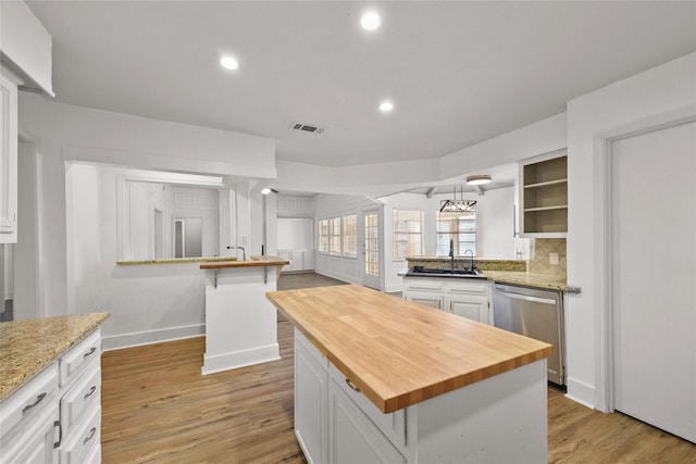 kitchen with butcher block counters, white cabinetry, stainless steel dishwasher, and a kitchen island