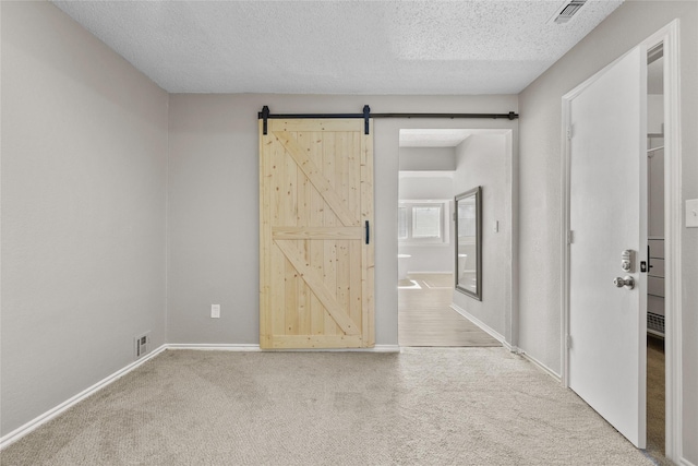 unfurnished room featuring carpet, a barn door, and a textured ceiling