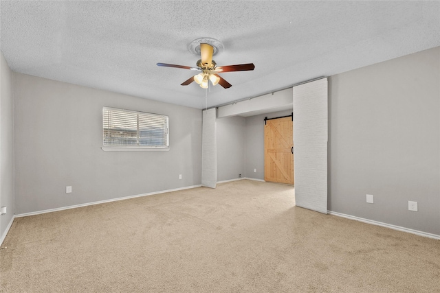 spare room with a textured ceiling, a barn door, and ceiling fan