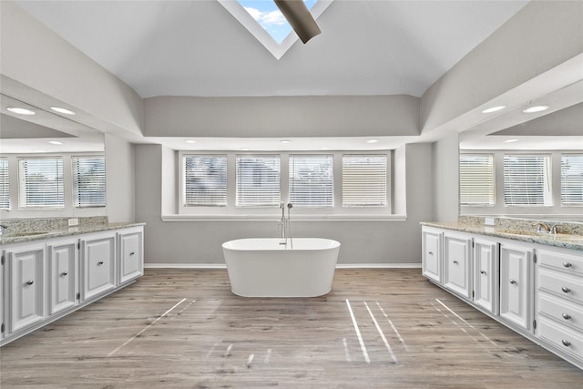 bathroom with a bath, hardwood / wood-style floors, vanity, and a skylight