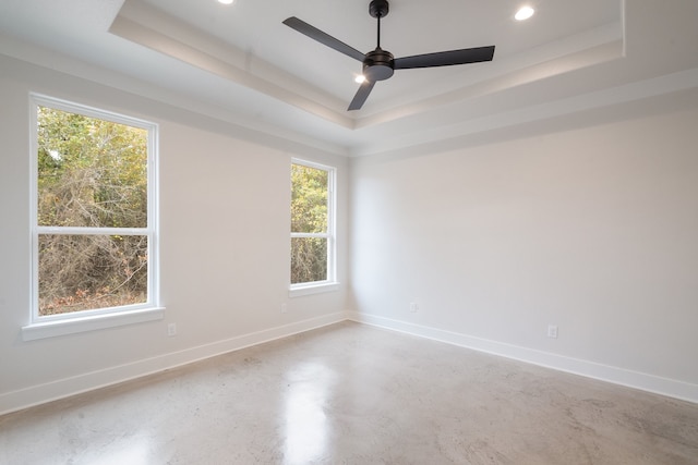 spare room featuring concrete floors, a tray ceiling, and ceiling fan