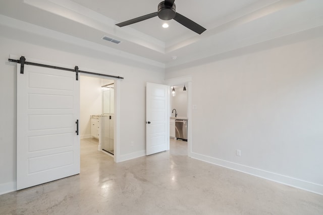 unfurnished bedroom featuring ceiling fan, a barn door, connected bathroom, and a tray ceiling