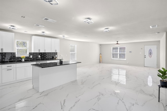 kitchen featuring sink, tasteful backsplash, a textured ceiling, a kitchen island with sink, and white cabinets