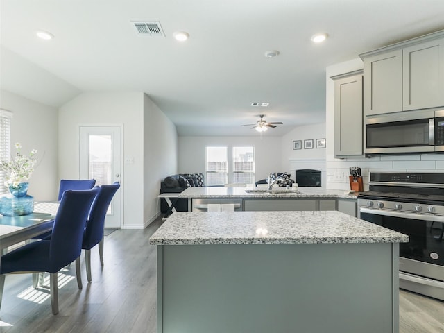 kitchen with stainless steel appliances, a kitchen island, backsplash, and light stone counters