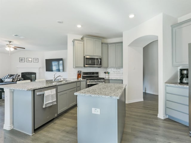 kitchen with light stone countertops, gray cabinets, stainless steel appliances, and a center island