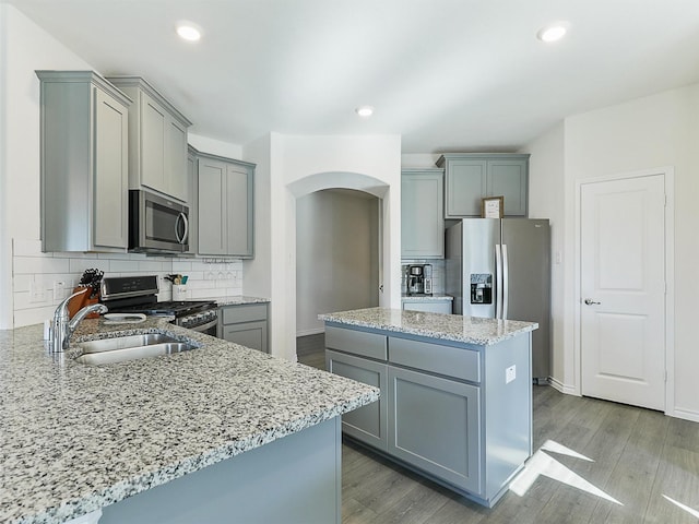 kitchen with light stone counters, appliances with stainless steel finishes, gray cabinets, and a center island