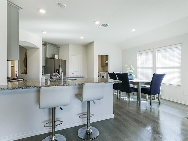 kitchen with gray cabinets, stone counters, a kitchen breakfast bar, independent washer and dryer, and stainless steel fridge with ice dispenser