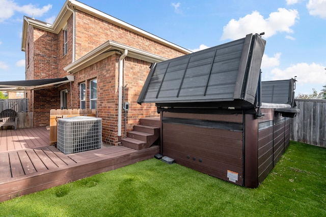 back of house with central air condition unit, a wooden deck, a lawn, and a hot tub