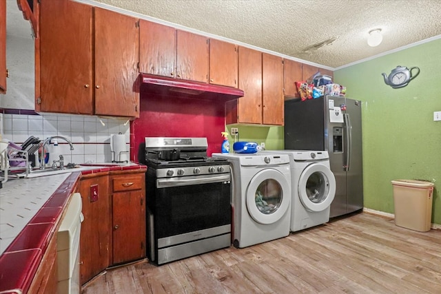 kitchen with washer and clothes dryer, appliances with stainless steel finishes, ornamental molding, light hardwood / wood-style floors, and tile countertops