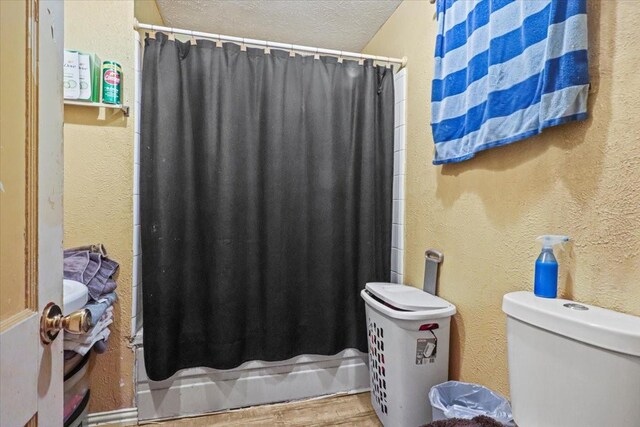 bathroom with wood-type flooring, curtained shower, a textured ceiling, and toilet