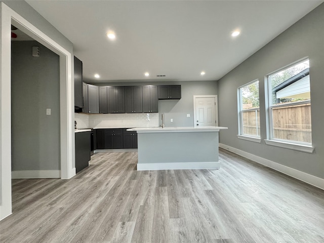 kitchen featuring sink, light wood-type flooring, backsplash, and an island with sink