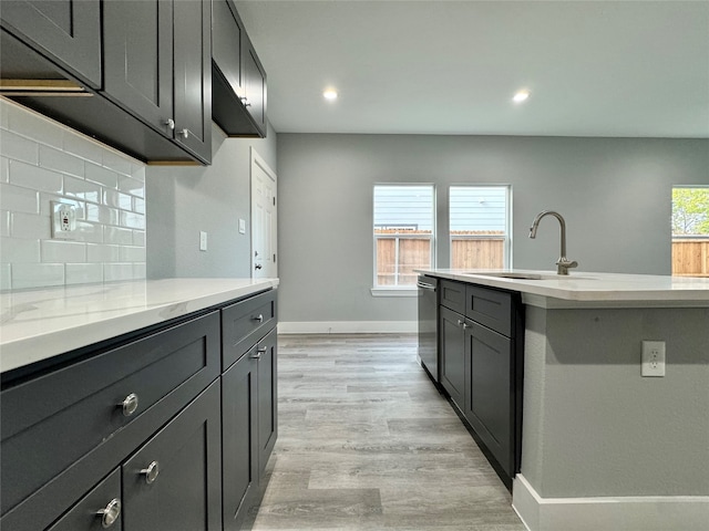 kitchen featuring tasteful backsplash, light stone counters, stainless steel dishwasher, sink, and light hardwood / wood-style flooring