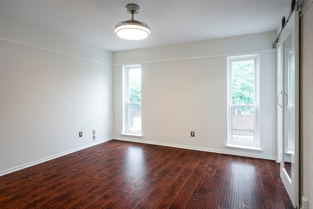 empty room featuring a barn door and dark hardwood / wood-style floors