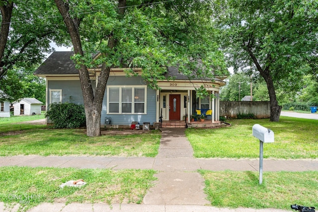 view of front of property with a porch, roof with shingles, a front yard, and fence